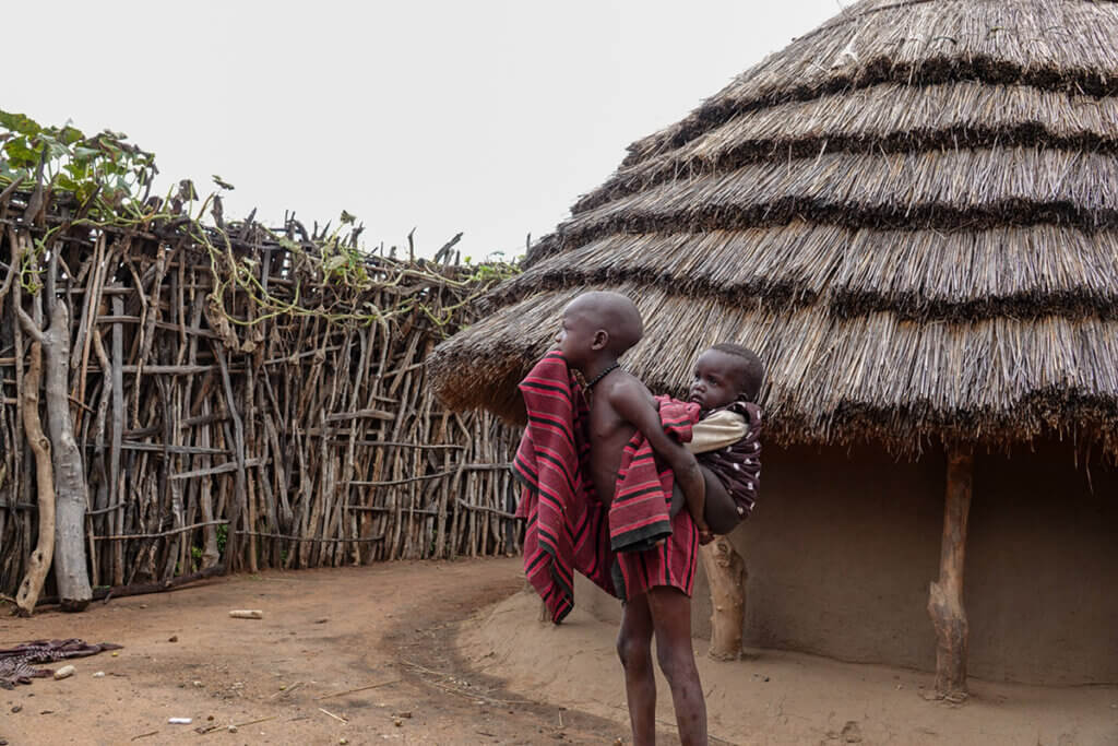 Karamoja Uganda: History, People and Culture of the Warrior Nomads Karamajong child with a baby on its back in Karamoja Uganda